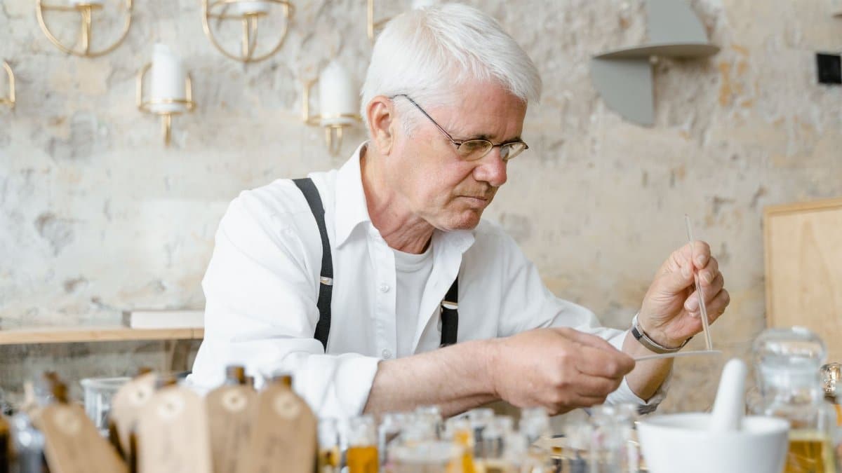 A senior man skillfully crafting perfumes in an artisanal setting, surrounded by glass bottles.
