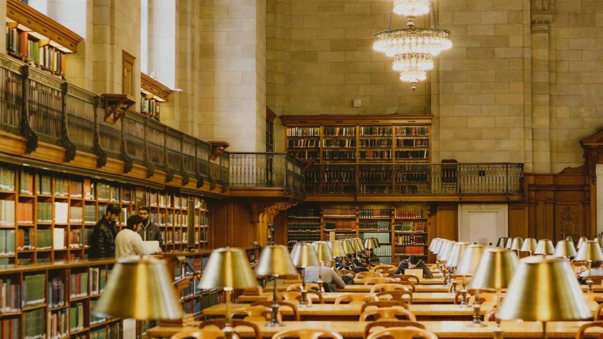 A bustling library with people reading and elegant chandeliers, perfect for studying.
