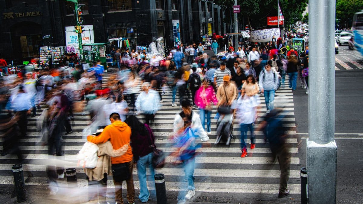 A bustling city street with a crowd of pedestrians crossing a zebra crossing, showcasing urban life.