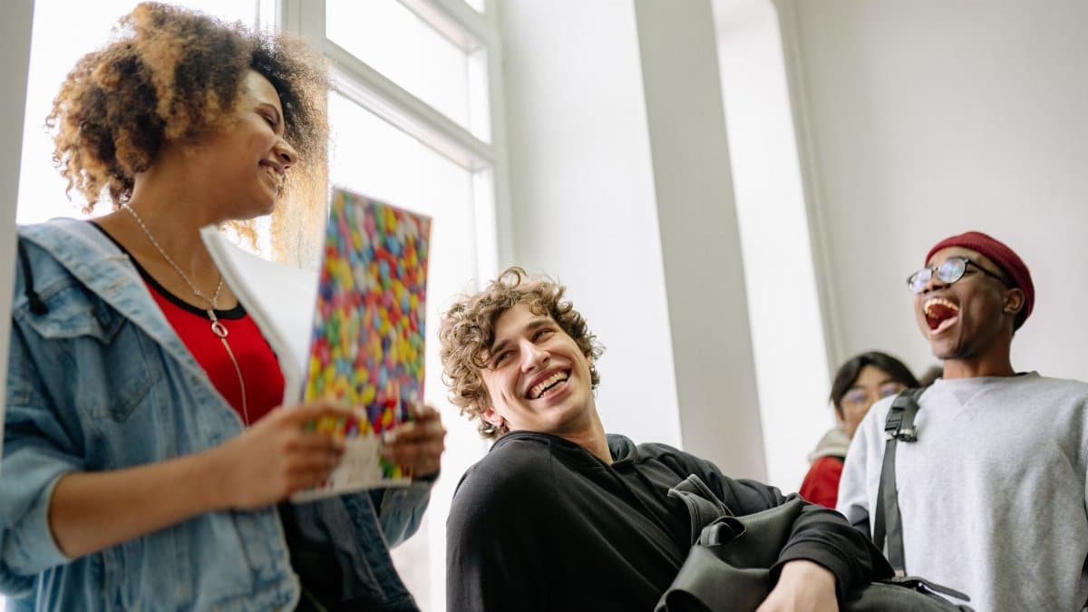 A group of cheerful students laughing and socializing in a bright college corridor.