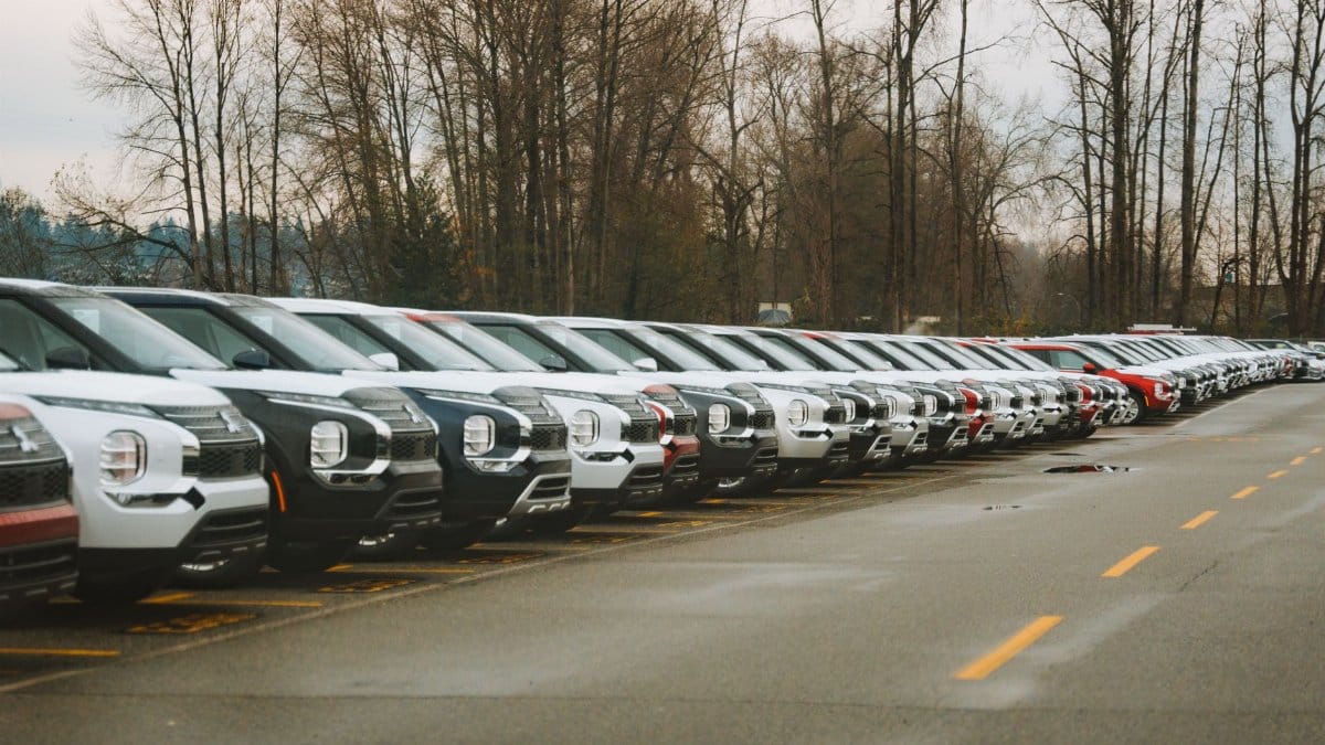 A line of brand new SUVs in an outdoor parking lot during a cloudy day.