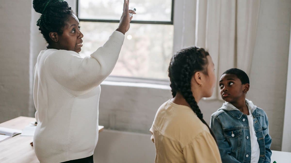 Clever African American woman explaining subject to attentive diverse pupils in modern classroom