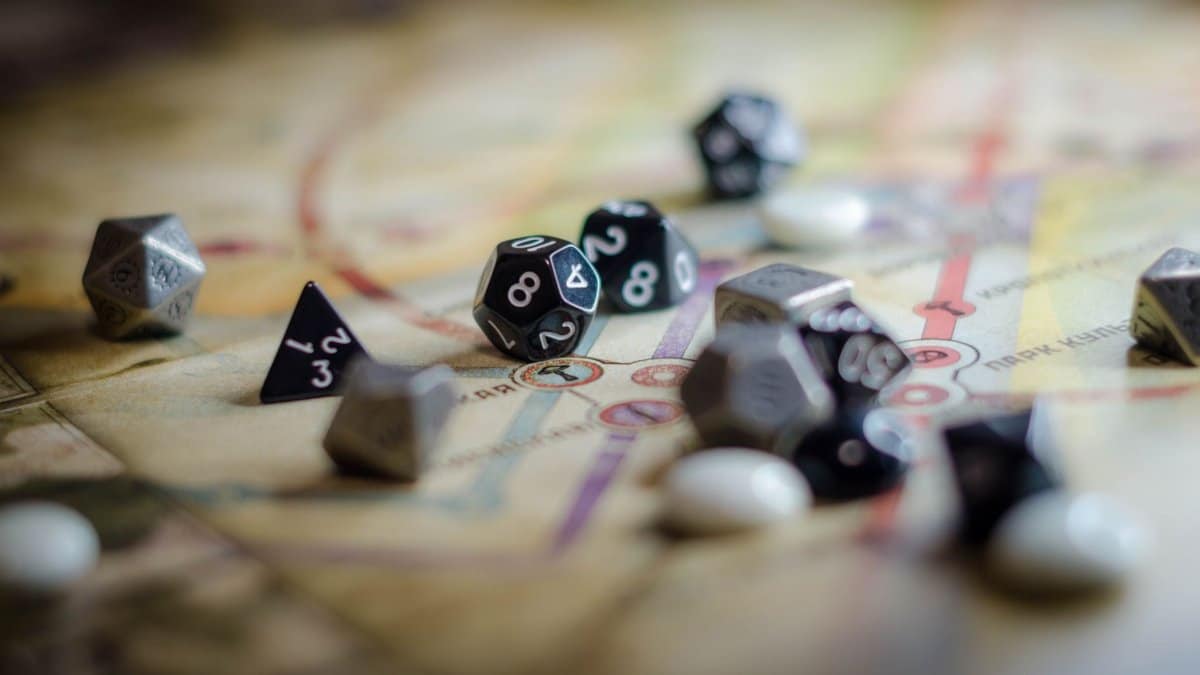 Focus on black and white polyhedral dice scattered on a board game map, suggesting strategy and chance.