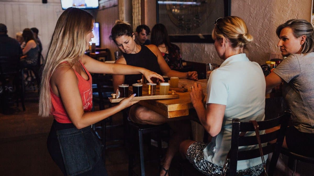 A group of women enjoying drinks served by a bartender in a cozy indoor bar environment.
