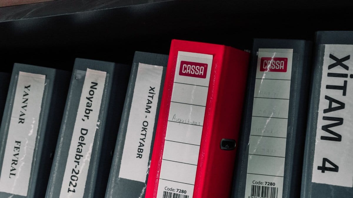 Color-coded office binders organized neatly in a storage shelf, featuring labels and a striking red binder.