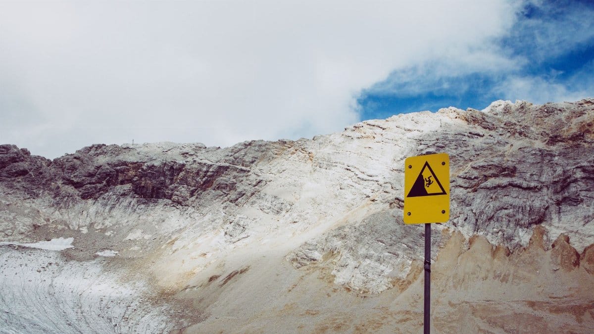 Mountainous terrain with a caution sign against falling rocks under a cloudy sky.