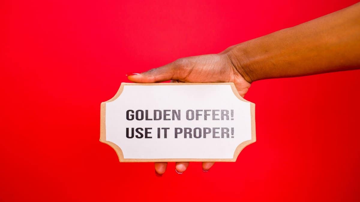 A hand holds a 'Golden Offer' sign on a vibrant red background, symbolizing deals and promotions.
