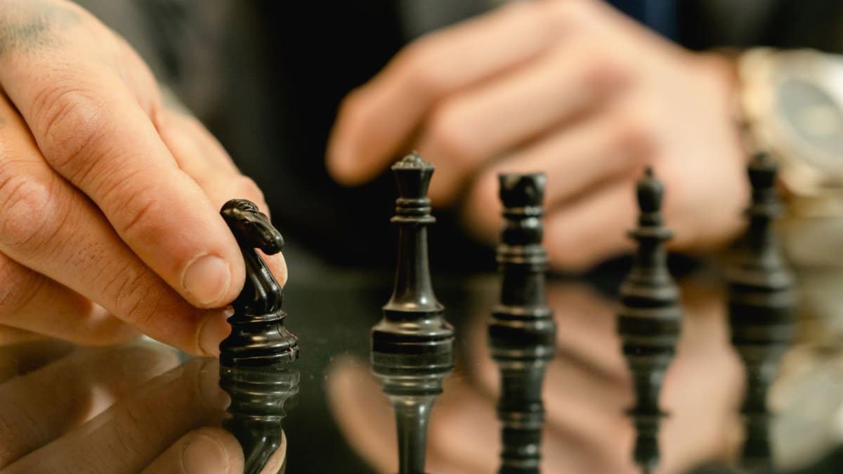 Close-up of a hand moving a chess piece on a reflective board, symbolizing strategy and decision-making.