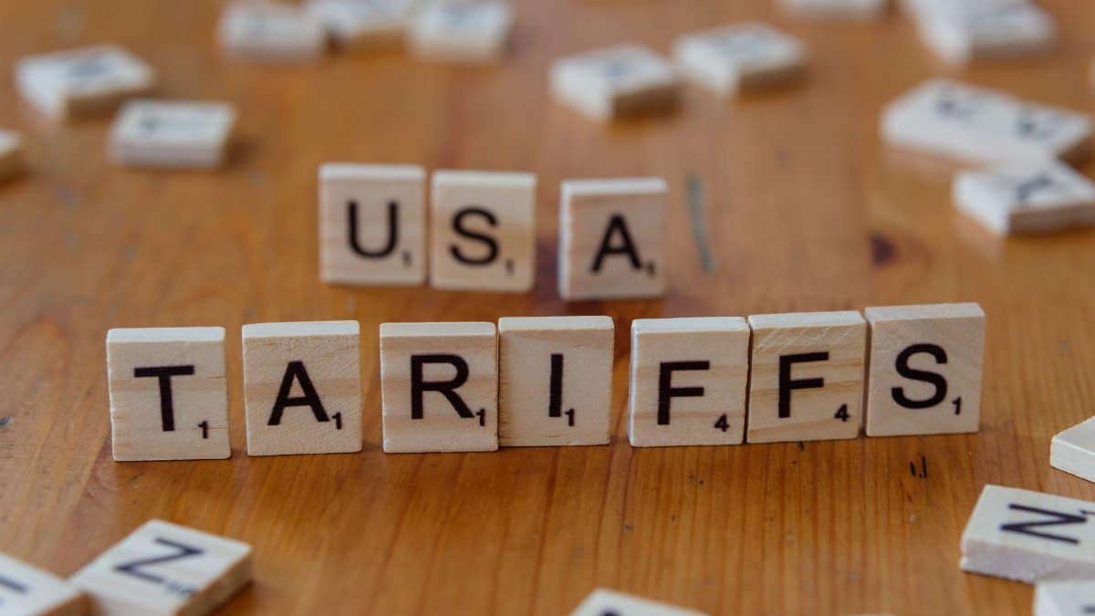 Wooden tiles spelling 'USA' and 'TARIFFS' on a wooden surface symbolizing trade issues.