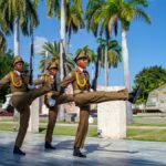 Military personnel performing a ceremonial march in Santiago de Cuba, surrounded by palm trees.