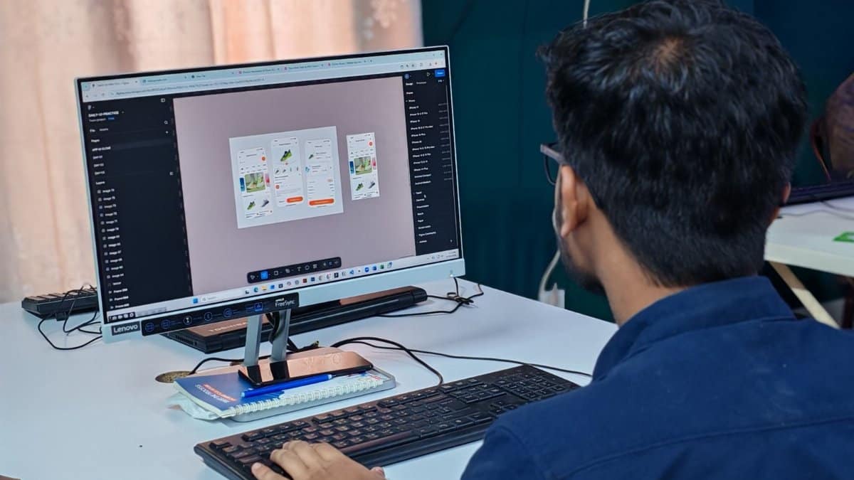 A young designer focused on creating user interfaces on a desktop computer in an office setting.