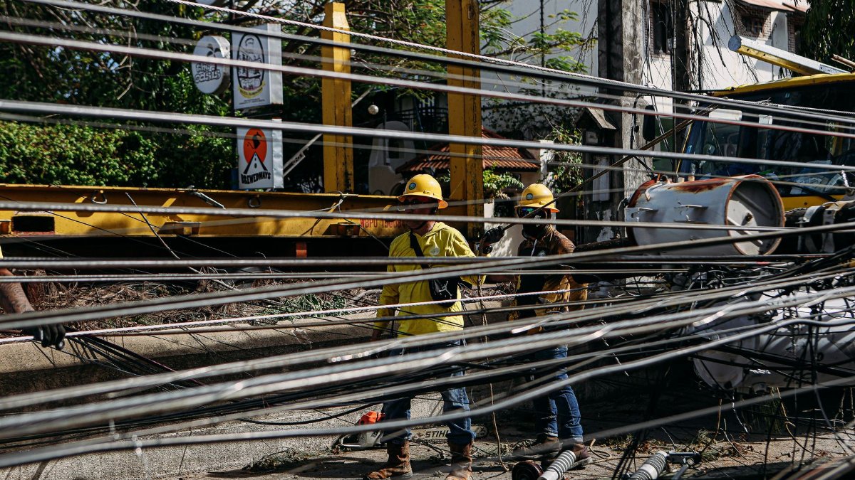 Utility workers in hard hats repair fallen power lines on a sunny day, ensuring electrical safety.