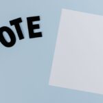 Flat lay of blank paper with 'VOTE' letters on light blue background, ideal for election-themed content.