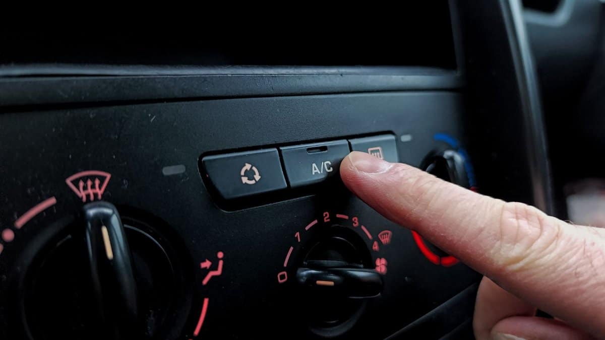 Close-up of a person adjusting a car's air conditioning system inside a vehicle cabin.