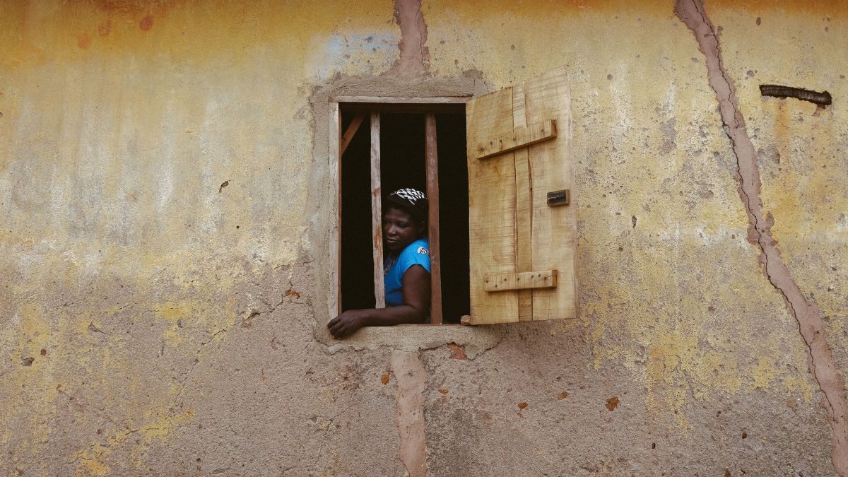 A woman gazes out of a rustic window in a traditional building in Ife, Nigeria.