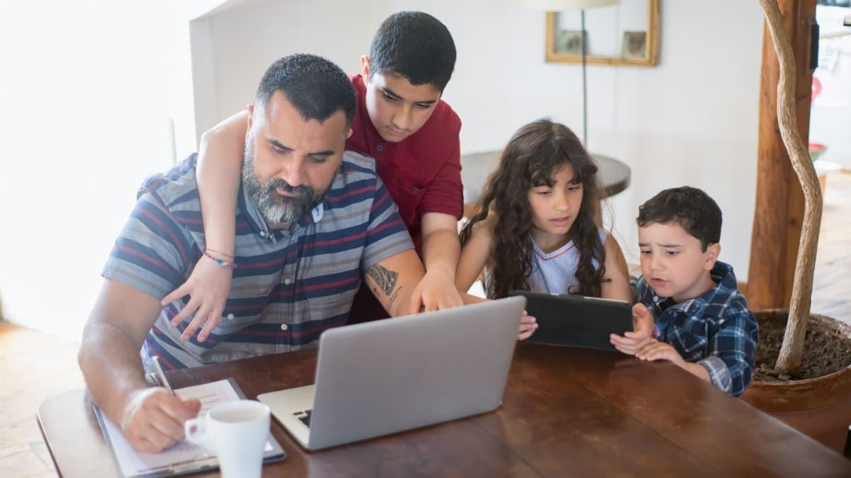 A father and his children engaged in activities with a laptop and tablet at home.