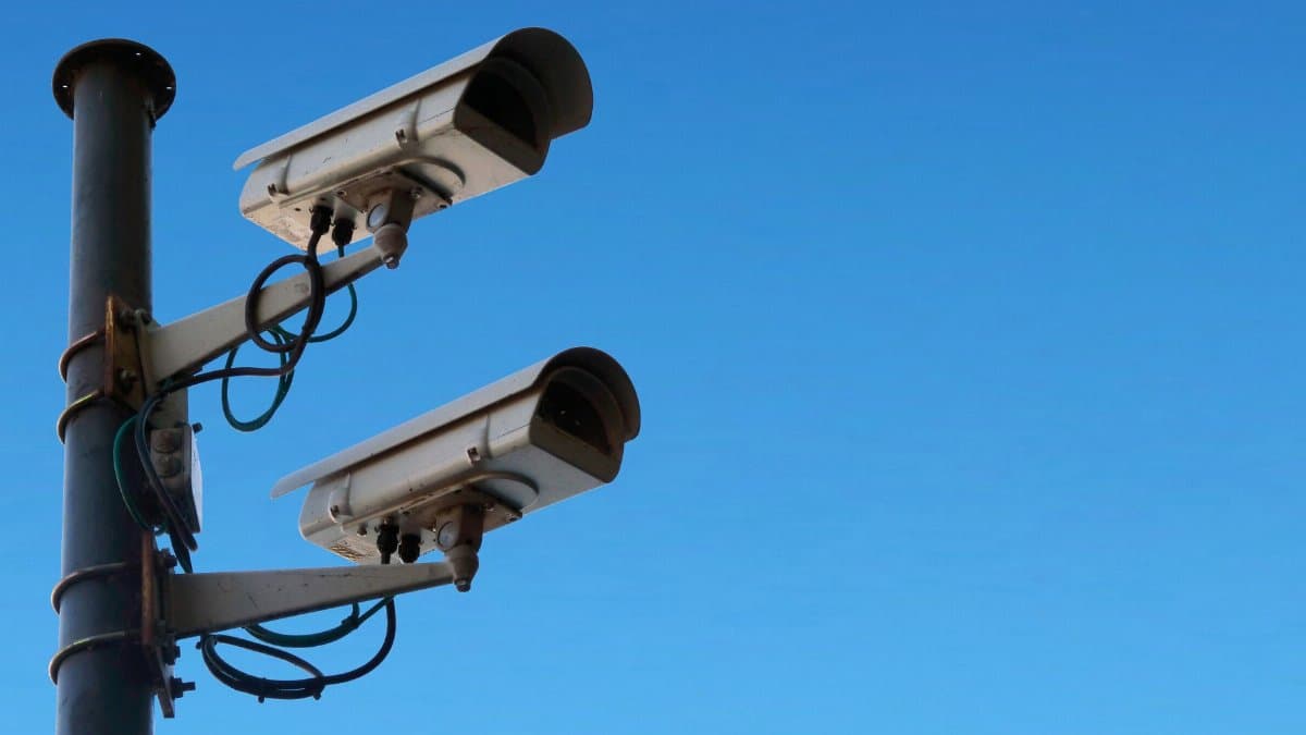 Low angle of security camera attached to black post located isolated on blue sky on sunny day in daytime outside