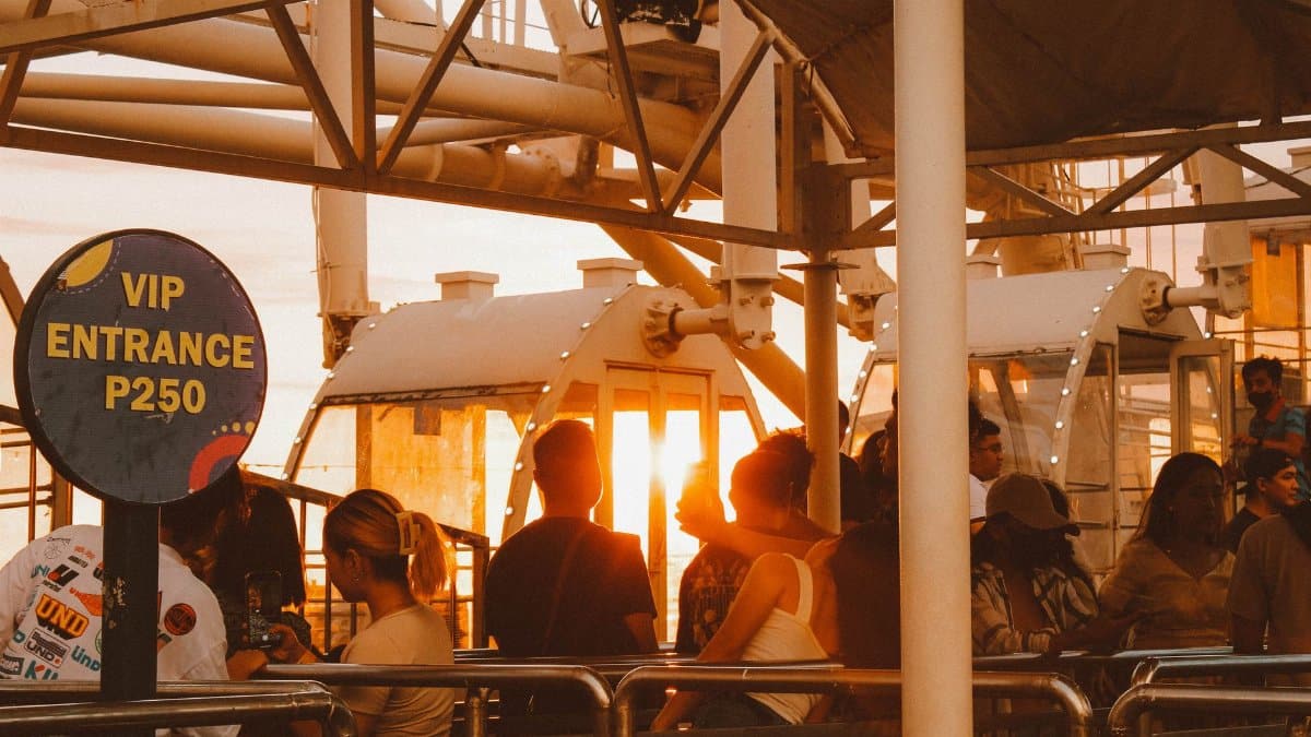 Tourists queuing for a ferris wheel ride at sunset with VIP entrance sign.