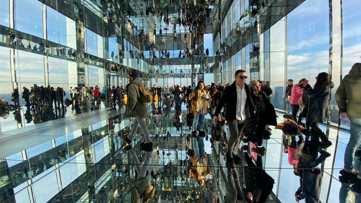 Crowded glass corridor with stunning reflections creating a mesmerizing illusion.