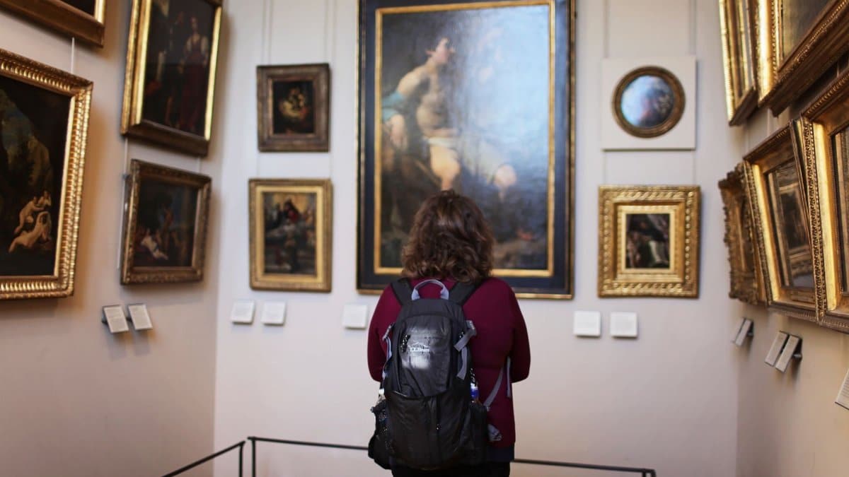 A visitor observes classic paintings in a tranquil museum gallery setting.