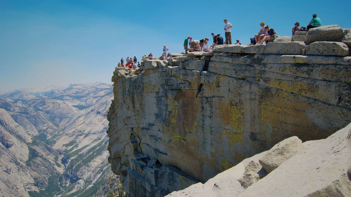 Hikers on the summit of Half Dome in Yosemite National Park, California, with stunning views.