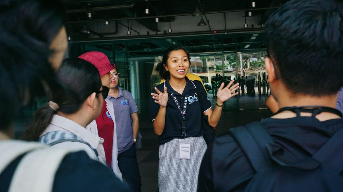 Tour guide leading a group tour, engaging visitors with gestures in an outdoor urban setting.