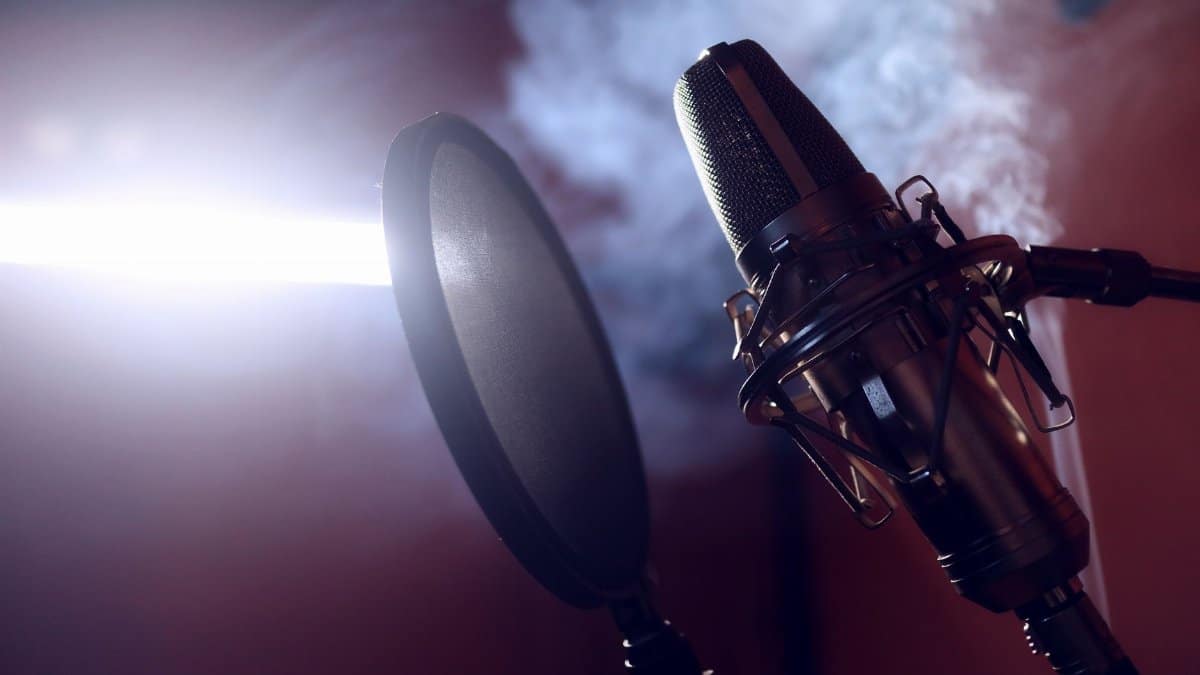 Close-up of a condenser microphone and pop filter in a smoke-filled recording studio.