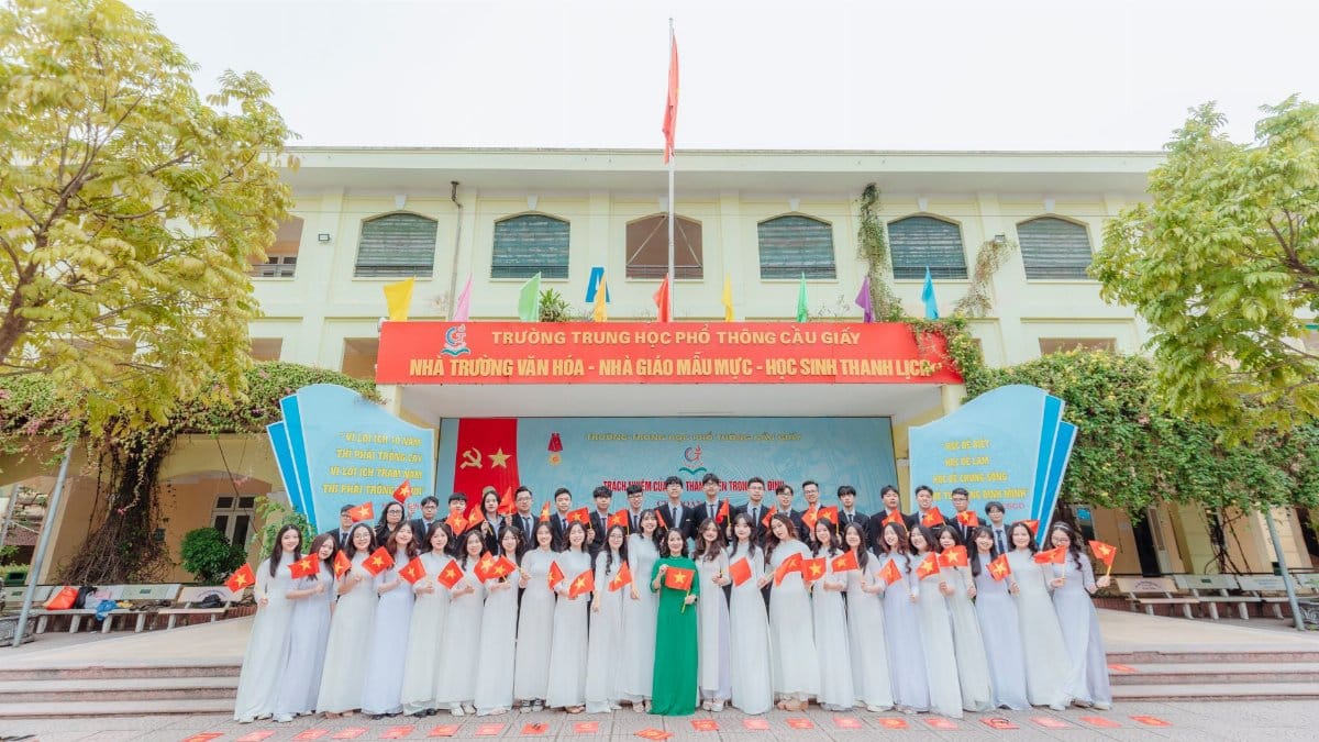 Students celebrating graduation with flags in front of a school in Vietnam.
