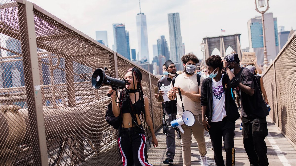 A diverse group of protesters march with megaphones on the Brooklyn Bridge, advocating for justice and equality.