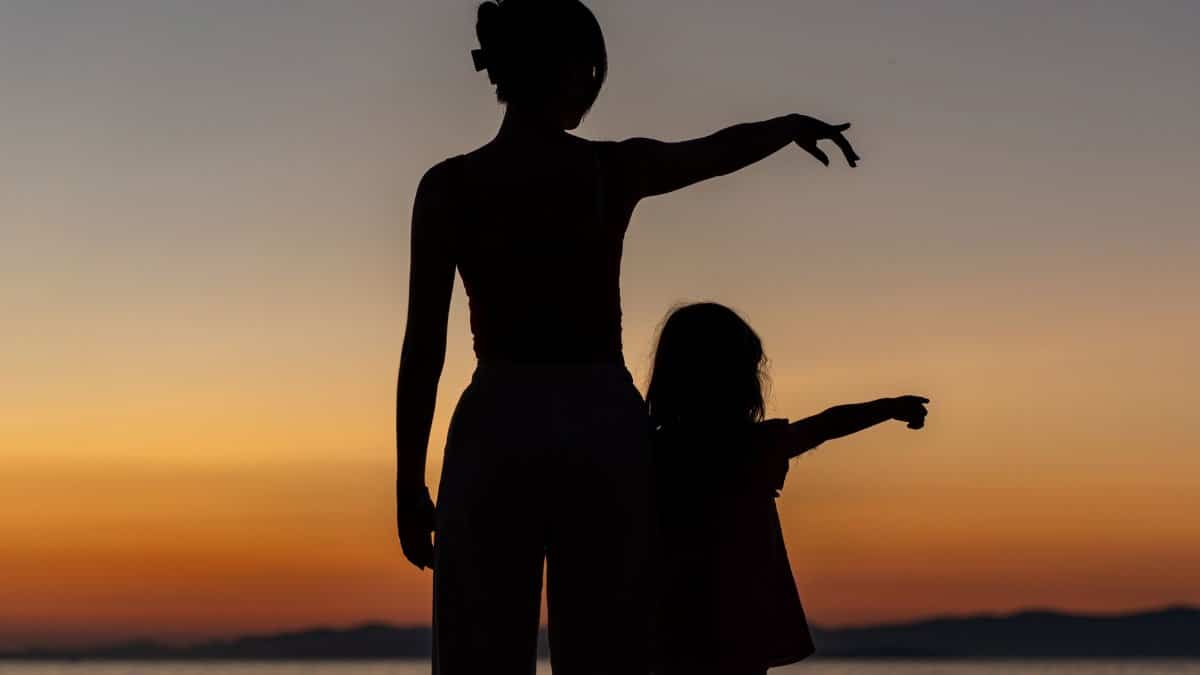 Silhouetted woman and child enjoying a serene sunset by the sea in Supetar.