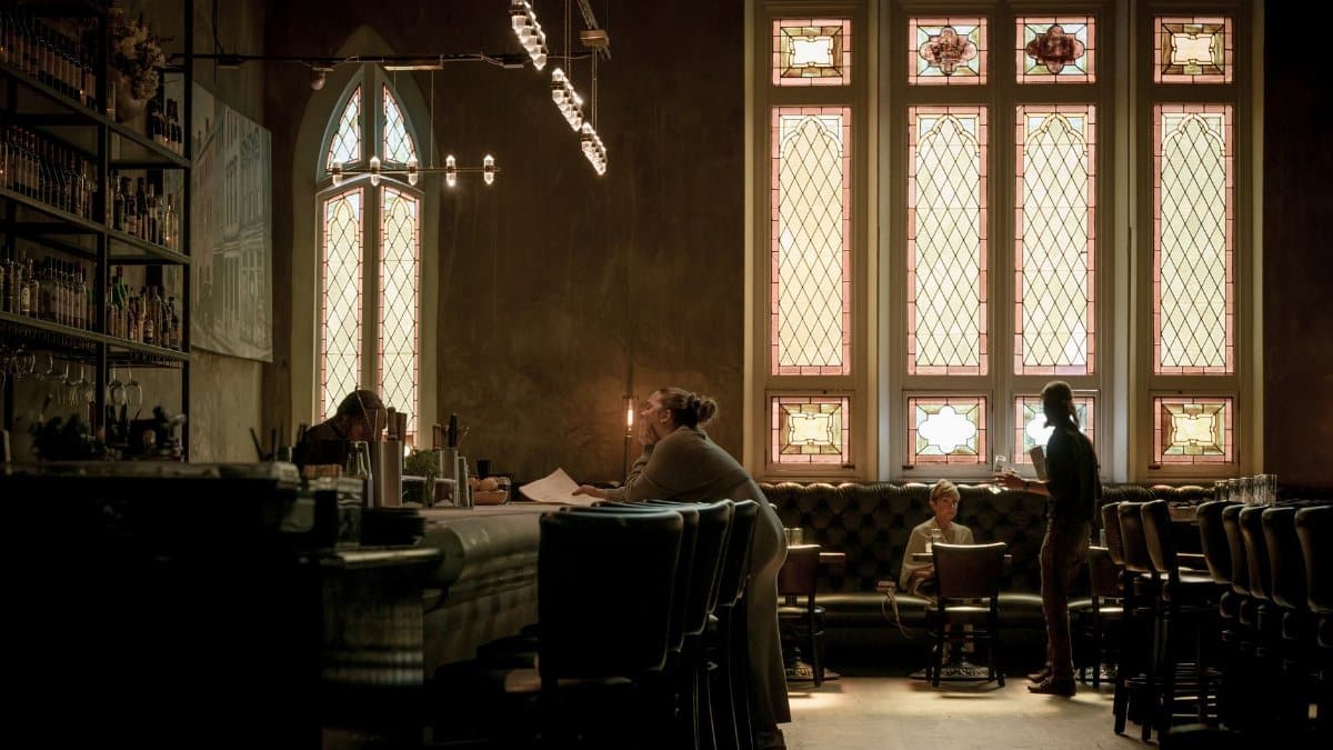 Elegant bar with stained glass windows and patrons, creating a cozy ambiance.
