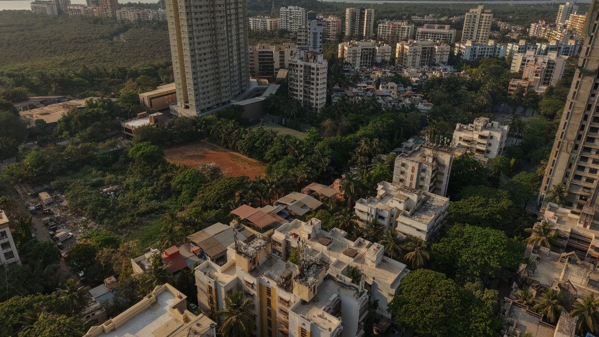 Aerial shot of dense residential skyscrapers in Mumbai, surrounded by green areas at dusk.
