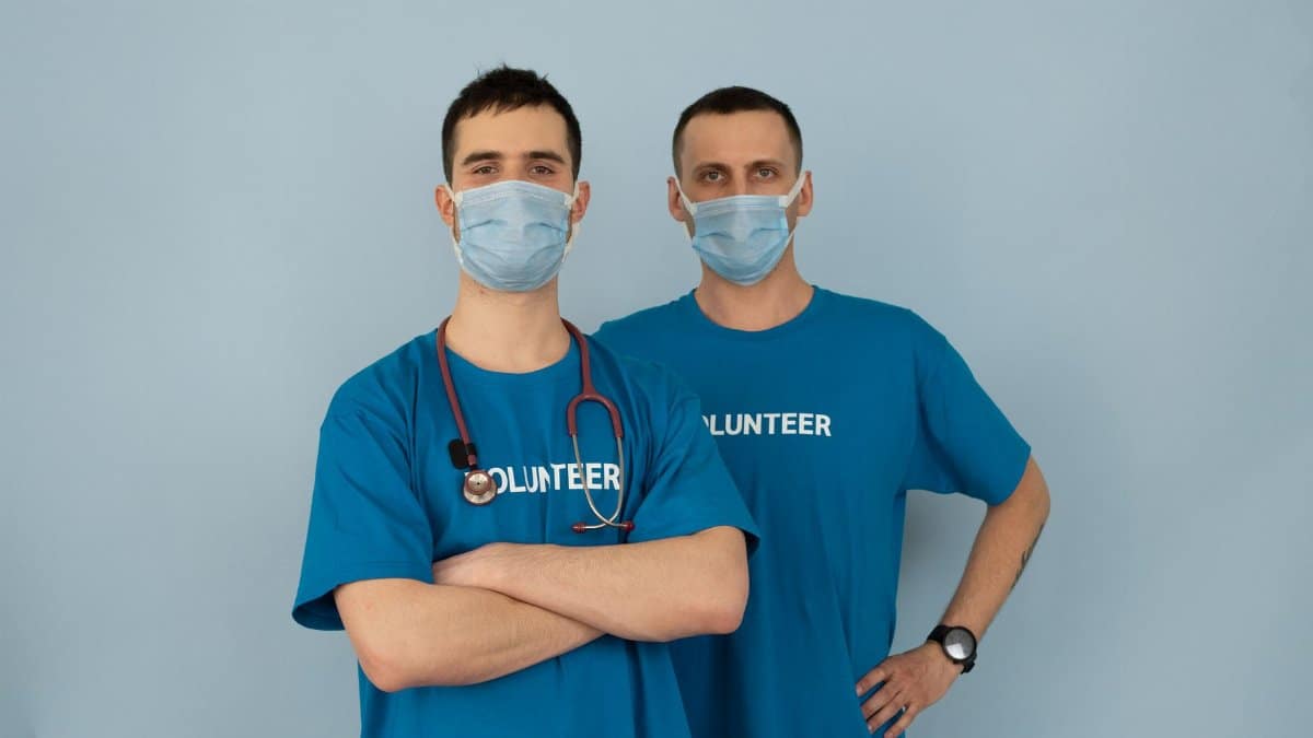 Two men in blue volunteer shirts and masks, symbolizing teamwork and safety.