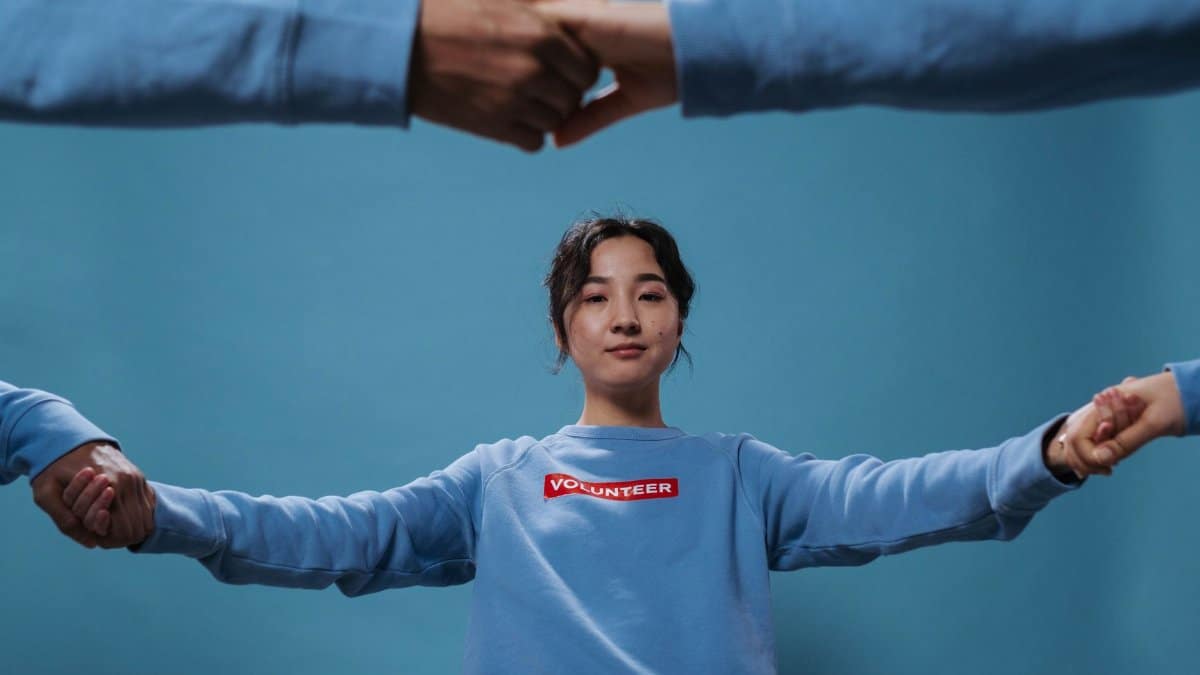 Asian woman in blue volunteer shirt holding hands in a circle, symbolizing teamwork and community.