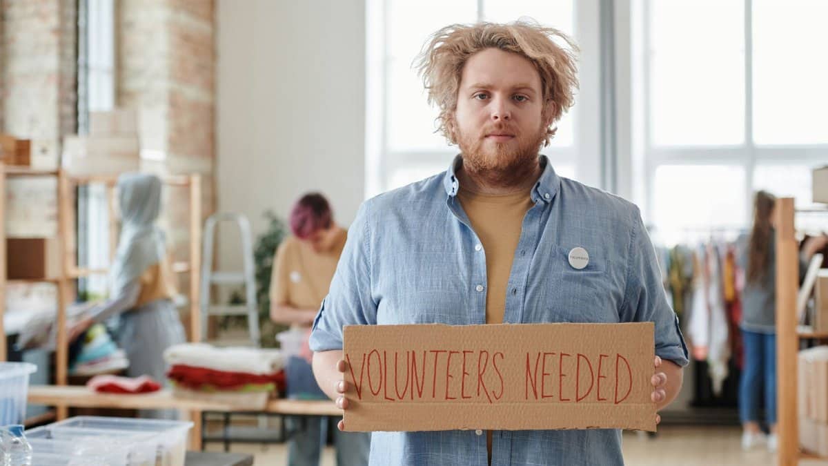 Man holding a sign for volunteer recruitment at a community center.