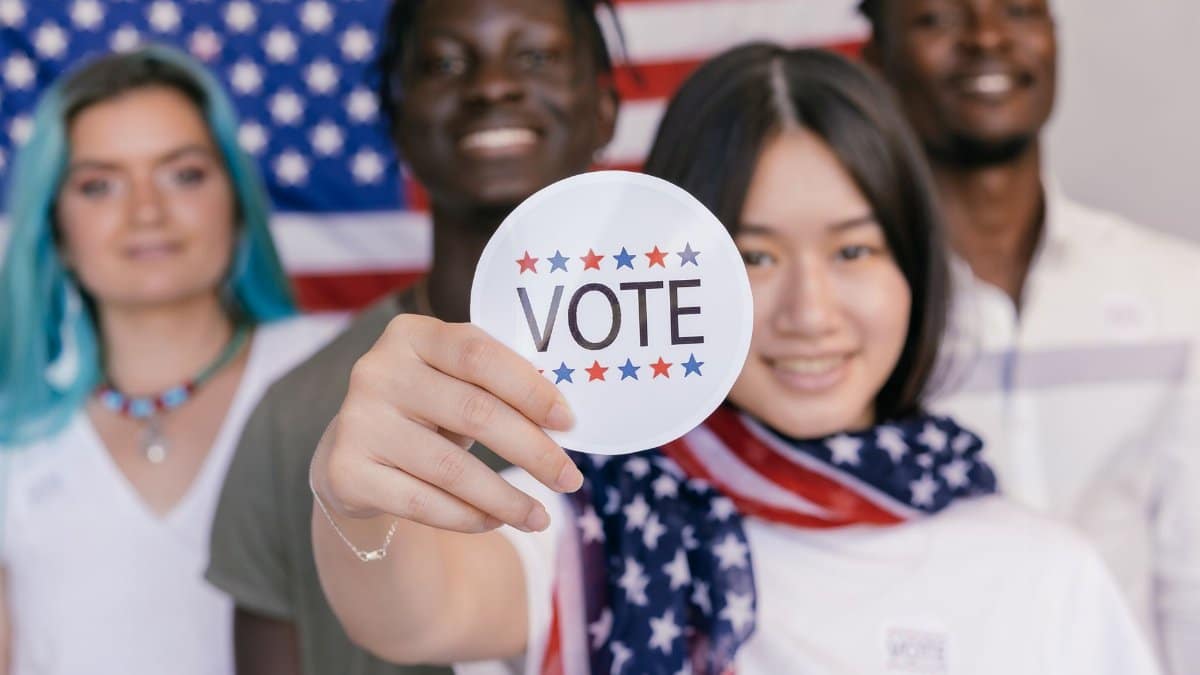 Group of diverse young adults promoting voting with a focus on a 'VOTE' sticker.
