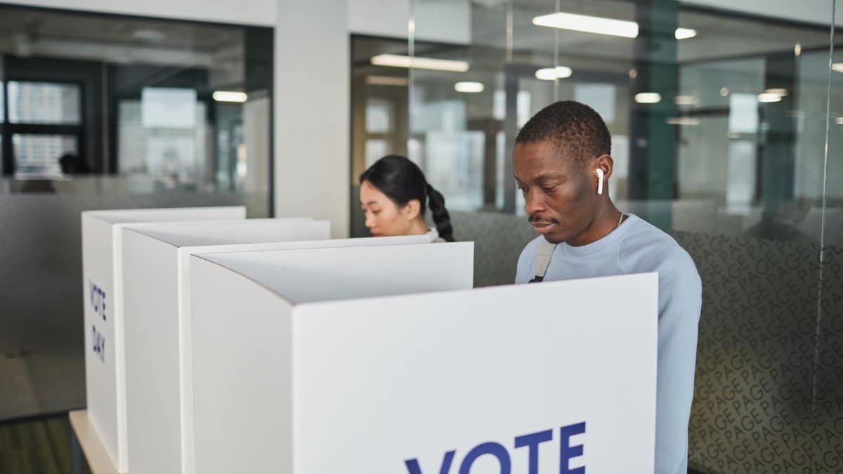 Two individuals casting votes in an indoor voting booth, emphasizing democracy.