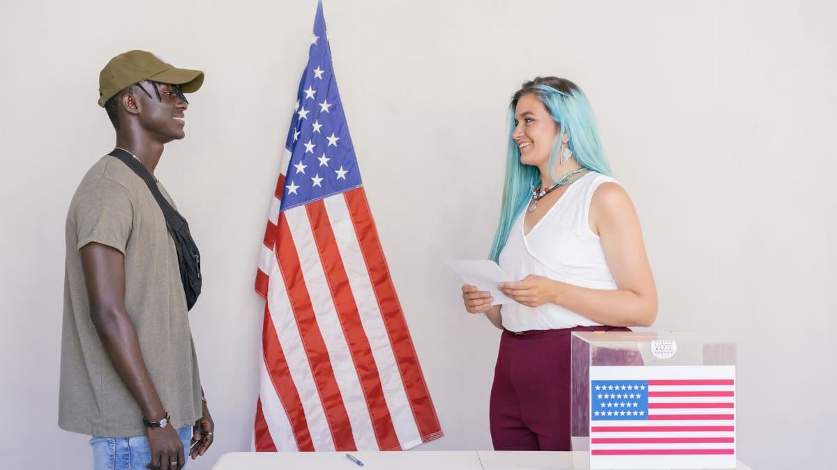 Two diverse young adults engaging in a voting process next to an American flag.
