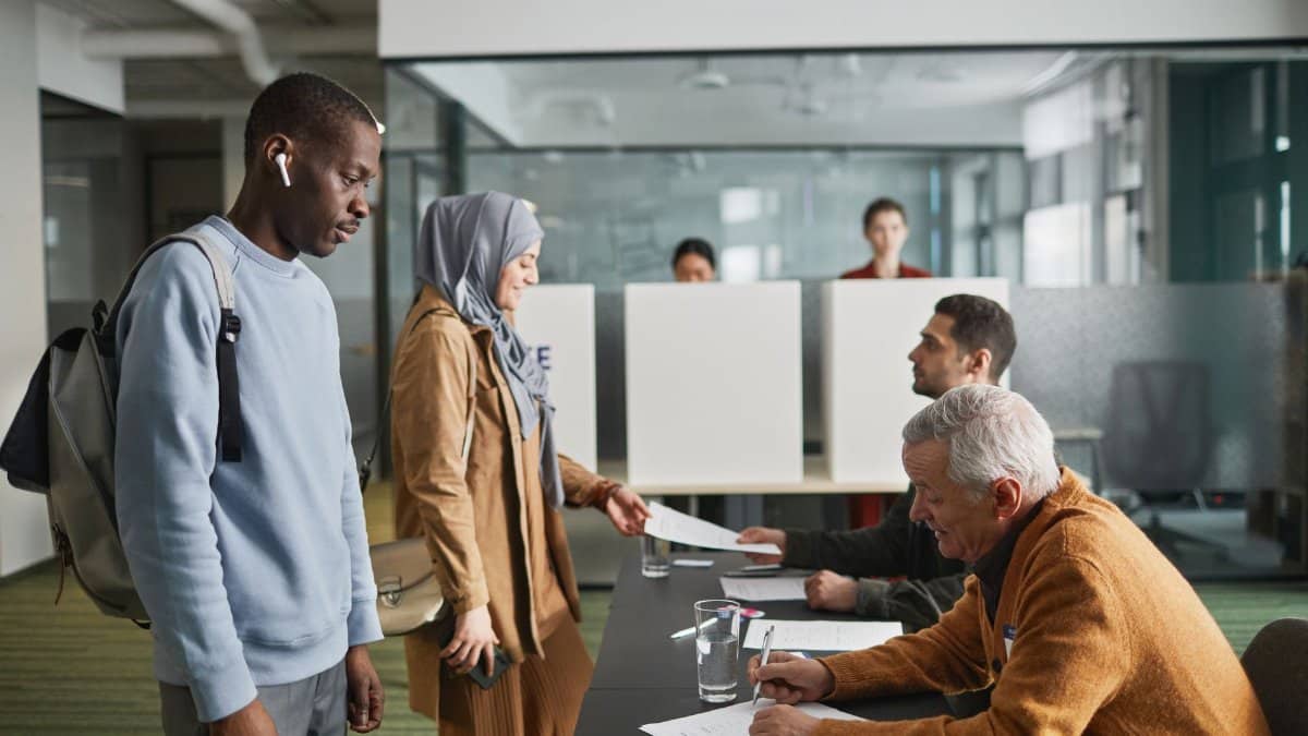 A diverse group of adults engaged in voting at an indoor polling station.