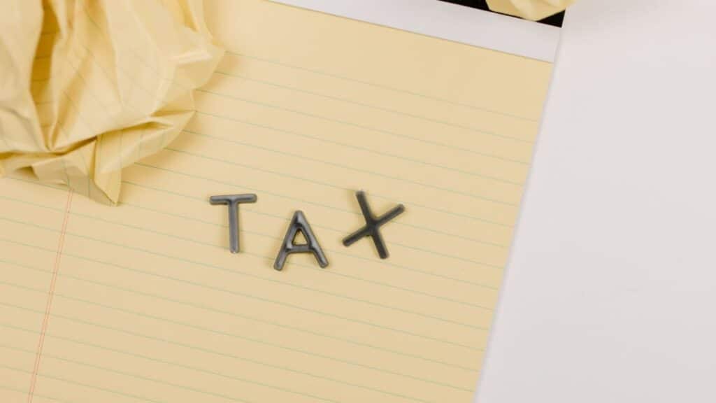 Close-up of a yellow lined paper with metal letters spelling 'tax', surrounded by crumpled paper.