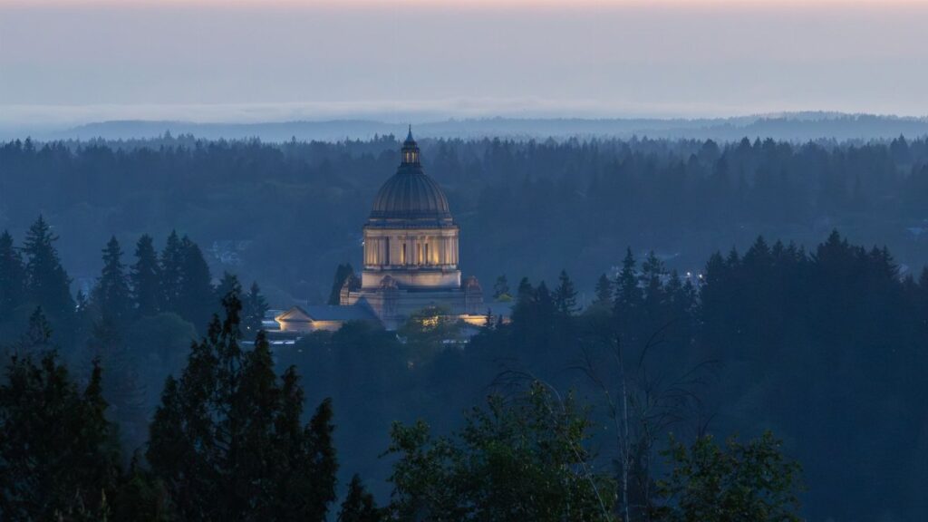 Dramatic view of the Washington State Capitol building in Olympia at dusk, surrounded by forest.