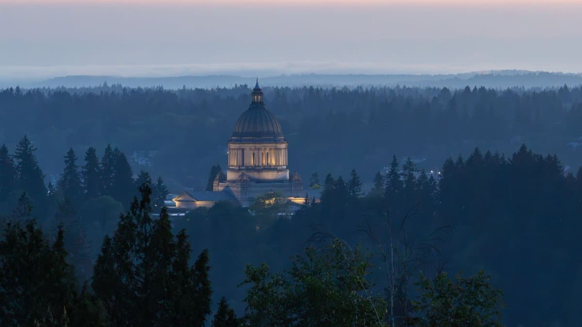 Dramatic view of the Washington State Capitol building in Olympia at dusk, surrounded by forest.