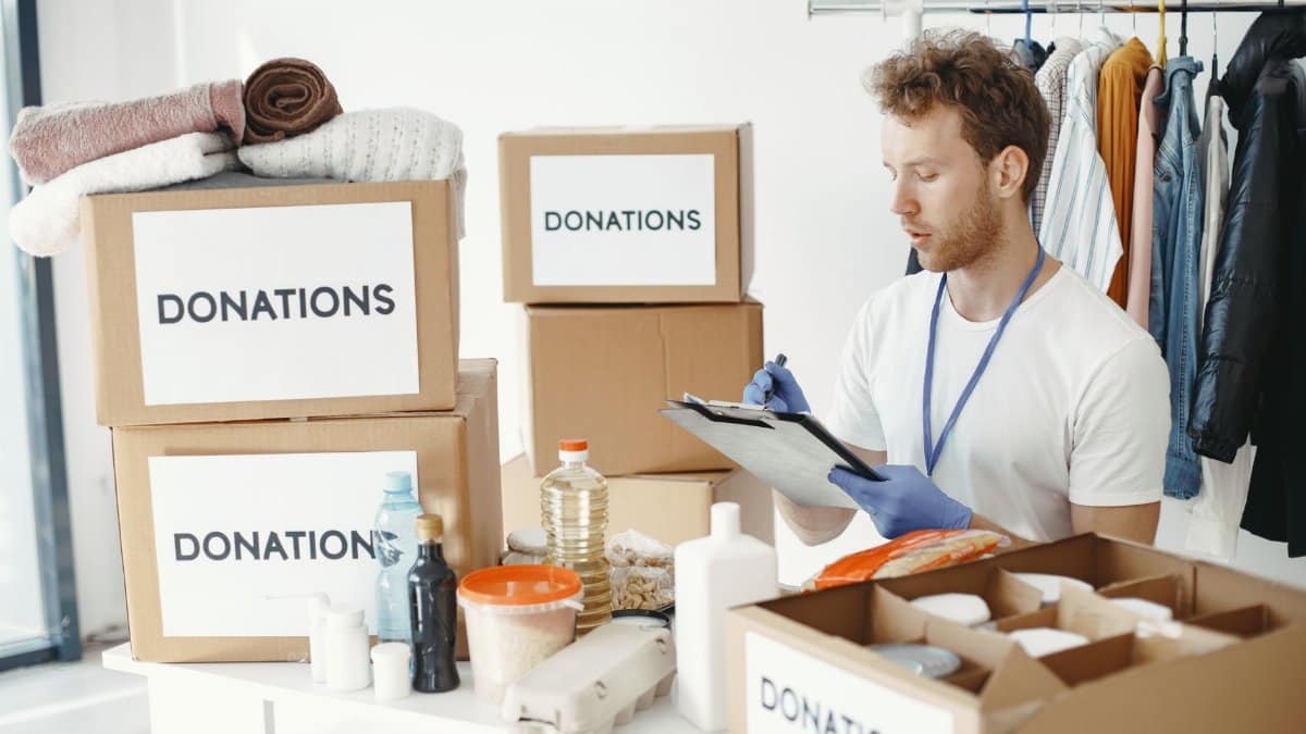 A man organizing donation boxes filled with clothes and food items at an NGO office.