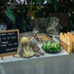 A welcoming cafe table set with Banh Mi ingredients and an inviting sign in a leafy atmosphere.