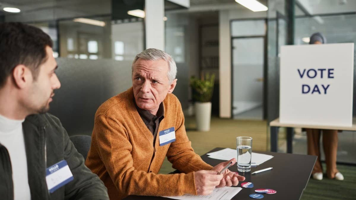 Two election officials discuss voting day logistics inside a modern office environment.