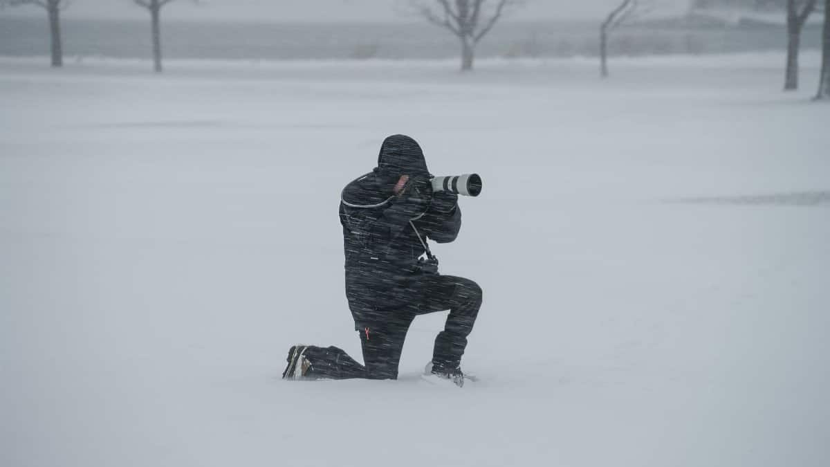 A dedicated photographer kneels in a snowy field, braving a winter storm to capture stunning images.