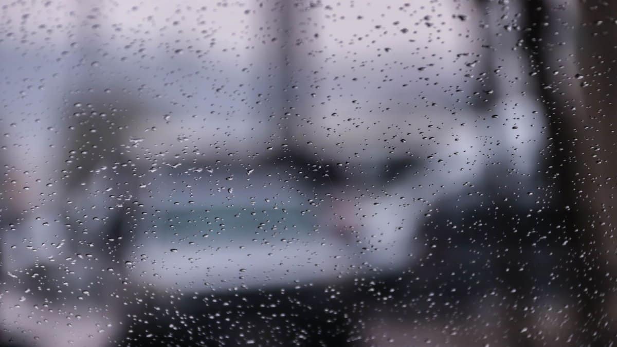 Rain on a glass window with a blurred view of a city and cars in the background, creating a moody atmosphere.