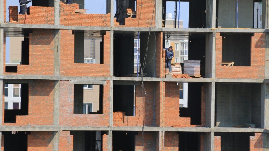 View of construction workers building brick walls on an unfinished urban apartment.