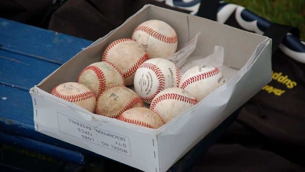 A box full of used baseballs sitting on a blue bench outdoors, perfect for sports enthusiasts.