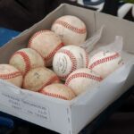 A box full of used baseballs sitting on a blue bench outdoors, perfect for sports enthusiasts.